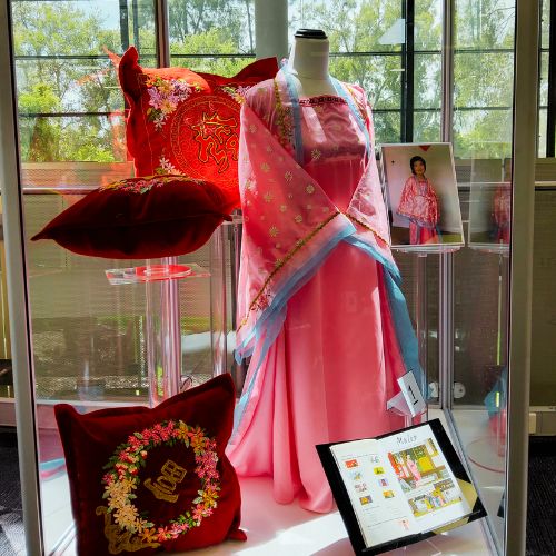 Clear display case containing pink hanfu and red embroidered cusions