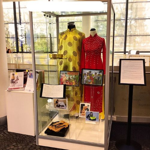 A clear display case showing two traditional Vietnamese wedding costumes, one red and one gold and traditional Vietnamese wooden clogs