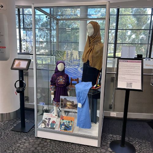 Glass display case containing adult and child mannequins wearing hijab, snowscape artwork in the background, dentristry outfit and picture books in the foreground