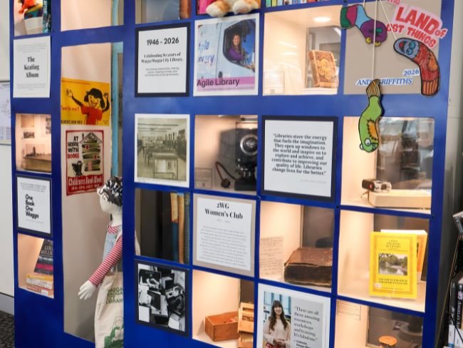 A set of display shelves with photographs, books, a mannequin, and a printed dates