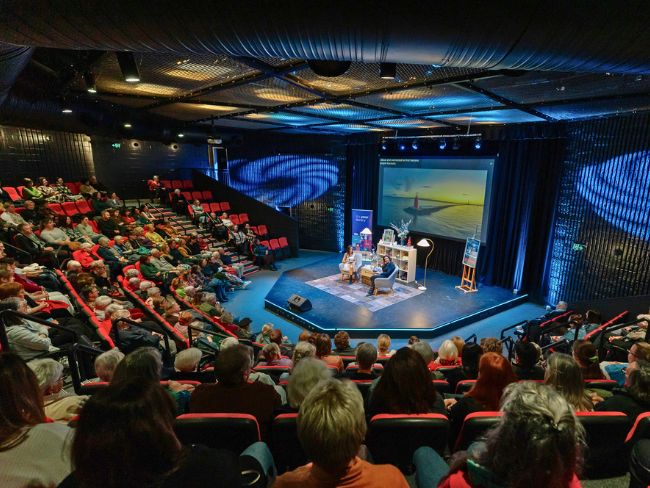 Louise and Irma seated on the Riverina Playhouse stage, as seen from the back of a nearly sold-out audience.