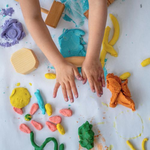 Two young hands are rolling and squishing colourful playdough