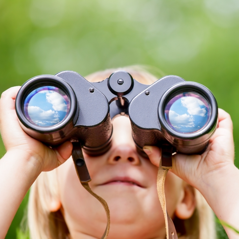 A photo of a young blonde child looking through binoculars.