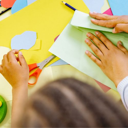 Seen from above, hands reach across paper and card on a table.
