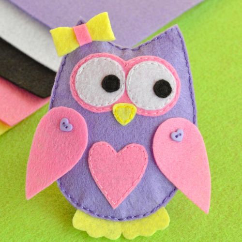 A cartoonish owl, made from pink purple and yellow pieces of felt, is looking owlishly to the right