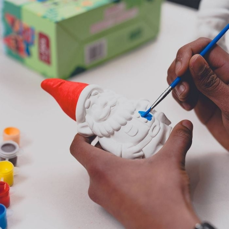 A close-up photo of someone painting a white garden gnome with blue paint.