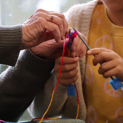 Two pairs of hands are collaborating with wool and knitting needles