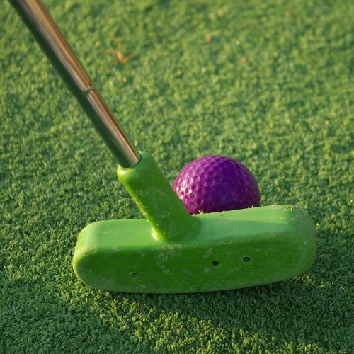 A bright green putter is cosying up to a bright purple golf ball