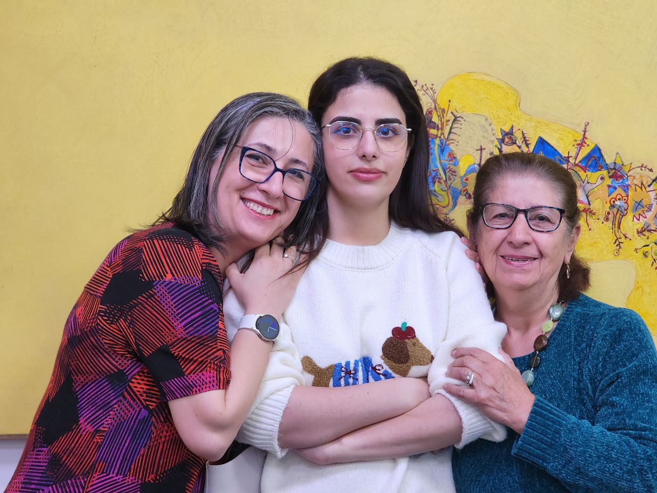 Photo of Shokoofeh, Niyousha and Maryam together in front of a yellow painting in the Library.