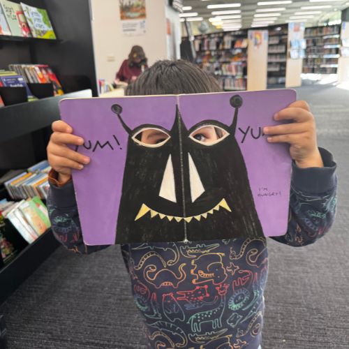 Eddie is a small boy holding a picture book up in front of his face so he can look through a silly monster's eyeholes