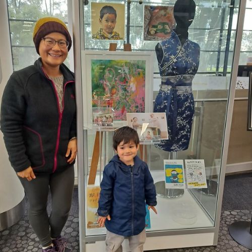 Valerie is smiling and standing to one side, while little Eddie stands in front, of the display cabinet containing their family's story